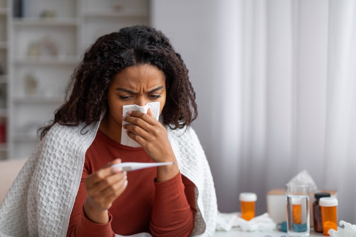 फोटो: बीमार काली महिला की नाक बह रही है और वह घर पर थर्मामीटर देख रही है